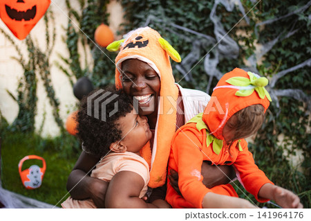 Mother embracing children celebrating Halloween wearing pumpkin hats Mother embracing children celebrating Halloween wearing pumpkin hats 141964176