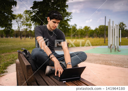 Young man using tablet as laptop on park bench 141964180