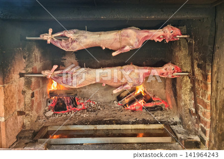 Two whole lambs roasting on a spit over an open fire 141964243
