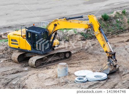 Large yellow excavator machine parked on construction site, concrete elements on ground, heavy equipment for earthmoving operations, building projects in progress Large yellow excavator machine parked on construction site, concrete elements on ground, heavy equipment for earthmoving operations, building projects in progress 141964746