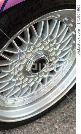 Detailed vertical photograph of silver multi-spoke wheel and tire on custom sports car, showcasing modern automotive design and car tuning aesthetics with vibrant fender detail and road surface. Detailed vertical photograph of silver multi-spoke wheel and tire on custom sports car, showcasing modern automotive design and car tuning aesthetics with vibrant fender detail and road surface. 141964902