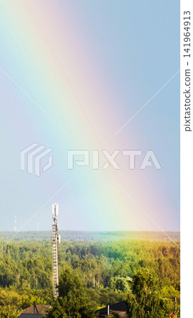 Rainbow arc stretching across clear blue sky above mobile telecommunication tower, lush green forest, and distant horizon, natural light illumination, weather phenomenon, vertical photo Rainbow arc stretching across clear blue sky above mobile telecommunication tower, lush green forest, and distant horizon, natural light illumination, weather phenomenon, vertical photo 141964913