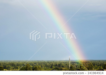 Bright colorful vibrant rainbow arc across expansive blue sky above lush green forest landscape featuring prominent modern mobile communication tower structure against horizon. Copy space Bright colorful vibrant rainbow arc across expansive blue sky above lush green forest landscape featuring prominent modern mobile communication tower structure against horizon. Copy space 141964914