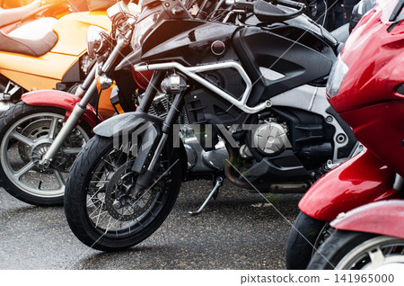 Multiple motorcycles parked on wet asphalt outdoors after rain, shiny surfaces reflect light, parked vehicles showcase modern design and travel freedom and adventure for riders. Multiple motorcycles parked on wet asphalt outdoors after rain, shiny surfaces reflect light, parked vehicles showcase modern design and travel freedom and adventure for riders. 141965000