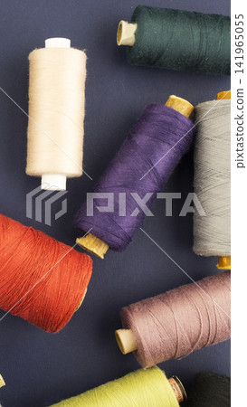 Multiple spools of colorful sewing thread, textile material for handcraft and art work, randomly arranged on dark blue fabric background, top view, studio shot vertical photo Multiple spools of colorful sewing thread, textile material for handcraft and art work, randomly arranged on dark blue fabric background, top view, studio shot vertical photo 141965055