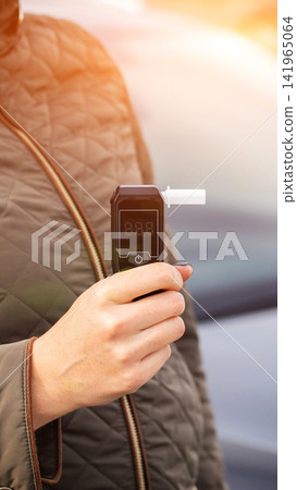Close up view of person hand holding digital alcohol breathalyzer with empty display ready for test outdoors during day time, car background blurred, safety concept, vertical photo Close up view of person hand holding digital alcohol breathalyzer with empty display ready for test outdoors during day time, car background blurred, safety concept, vertical photo 141965064