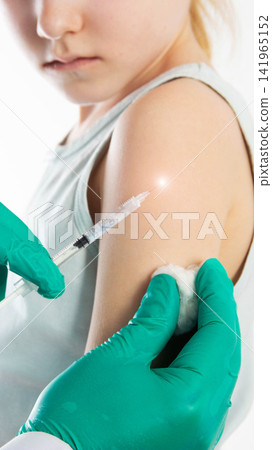 Young girl receives injection from person in green gloves administering vaccine to arm with syringe and cotton swab medical procedure shot prevention close-up studio background vertical photo Young girl receives injection from person in green gloves administering vaccine to arm with syringe and cotton swab medical procedure shot prevention close-up studio background vertical photo 141965152