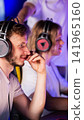 Young adult male wearing modern headphones concentrating on game screen, hand near mouth, focused expression, enjoying online computer game indoors at night with other gamers, vertical photo 141965160