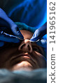 Doctor hands in blue gloves apply white strip on patient nose during medical examination procedure close up view dramatic lighting dark background, vertical photo, rhinoplasty, plastic surgery 141965162
