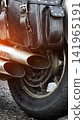 Close-up motorcycle rear section wet asphalt surface. Chrome exhaust pipes and dark leather saddlebag with metal studs. Detail of rear wheel and tire wet from rain on road. 141965191