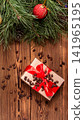 Christmas gift box with red ribbon and scattered pine nuts on rustic wooden table, adorned with pine branches, red ornament and pine cone, festive holiday background vertical photo 141965195