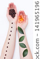 Caucasian hands hold roasted coffee beans and vibrant orange flower, parallel arms display raw coffee beans and fresh green leaves, symbolizing natural elements and daily routines, vertical photo 141965196