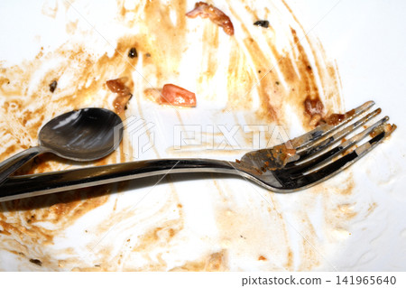 Close up of a messy dirty used white plate with cutlery on 141965640