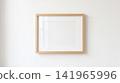Blank horizontal wooden picture frame hanging flat against smooth white interior wall providing empty copy space for custom photography exhibition artwork 141965996