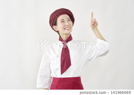 A female pastry chef points upwards. A female pastry chef points upwards. 141966069