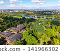 Drone view of Herrenkrug pedestrian bridge crossing Elbe River in Magdeburg, surrounded by green parkland and urban scenery. Summer cityscape shows waterfront, trees, architecture and transport links 141966302
