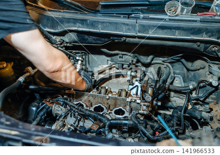 Hands of a mechanic repairing a vehicle under the raised hood in a professional garage workshop, auto service concept Hands of a mechanic repairing a vehicle under the raised hood in a professional garage workshop, auto service concept 141966533