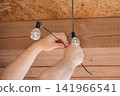 Close-up of human hands hanging a warm string of decorative light bulbs from the ceiling, home interior decoration concept 141966541