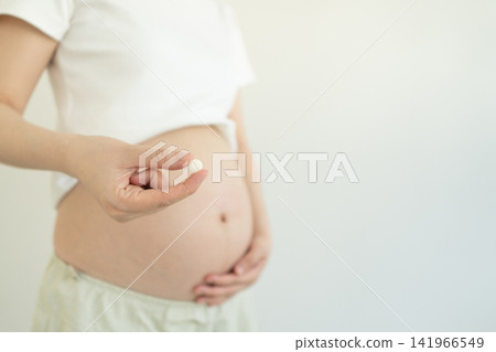 Pregnant woman holding dietary supplement pill against white background. Maternity prenatal care concept Pregnant woman holding dietary supplement pill against white background. Maternity prenatal care concept 141966549