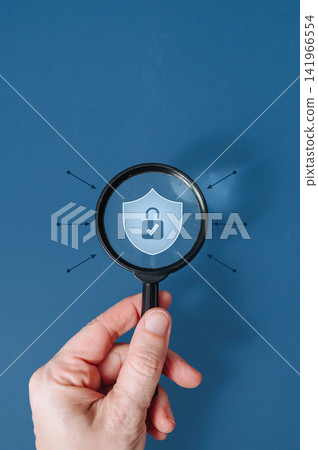 Hand holding magnifying glass over protective shield icon on blue background, data security and insurance concept Hand holding magnifying glass over protective shield icon on blue background, data security and insurance concept 141966554