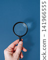 Hand holding a classic magnifying glass against a blue background with copy space, search and discovery concept 141966555