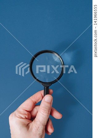 Hand holding a classic magnifying glass against a blue background with copy space, search and discovery concept Hand holding a classic magnifying glass against a blue background with copy space, search and discovery concept 141966555