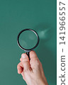 Hand holding a classic magnifying glass against a solid green background with copy space, ecological research concept 141966557