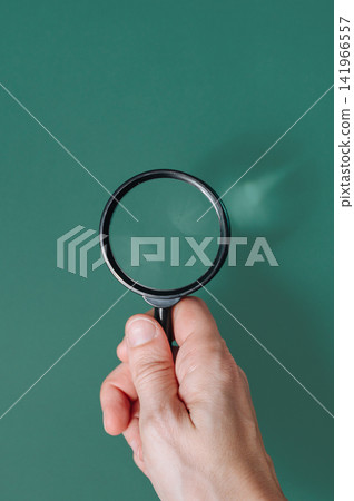 Hand holding a classic magnifying glass against a solid green background with copy space, ecological research concept Hand holding a classic magnifying glass against a solid green background with copy space, ecological research concept 141966557
