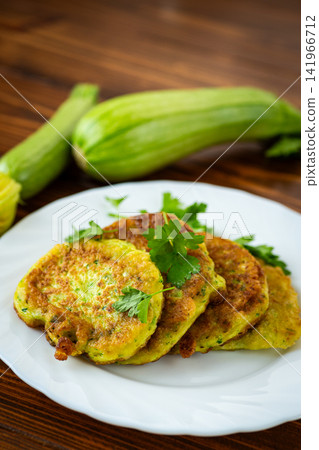 Crispy homemade zucchini fritters with fresh squash on rustic kitchen background Crispy homemade zucchini fritters with fresh squash on rustic kitchen background 141966712