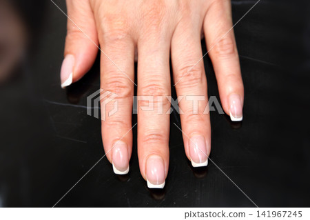 Receiving Professional Manicure in Modern Salon. Beautiful, well-groomed women's hands with elegant nails against a dark background. Beauty salon concept: manicures, pedicures. Receiving Professional Manicure in Modern Salon. Beautiful, well-groomed women's hands with elegant nails against a dark background. Beauty salon concept: manicures, pedicures. 141967245
