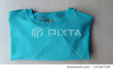 Folded teal crew neck sweater on light wood surface Folded teal crew neck sweater on light wood surface 141967299