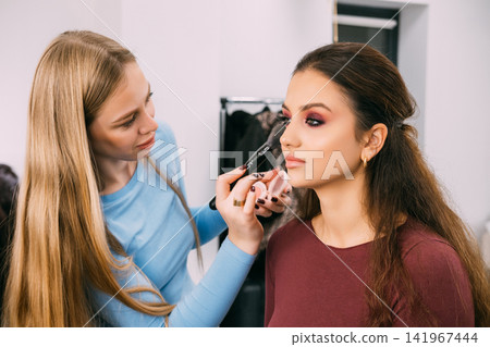Beauty face. Professional makeup. Female cosmetologist master applying cosmetic product for client skin treatment in salon. Beauty face. Professional makeup. Female cosmetologist master applying cosmetic product for client skin treatment in salon. 141967444