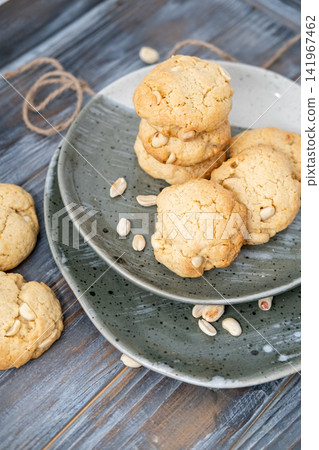 Baked cookies. Tasty food. Golden round treats served on rustic plate with scattered peanut ingredient on wooden table background. Baked cookies. Tasty food. Golden round treats served on rustic plate with scattered peanut ingredient on wooden table background. 141967462