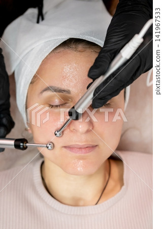 Face microcurrent. Skin therapy. Professional woman cosmetologist hands using modern aesthetic device for relaxing lifting procedure. Face microcurrent. Skin therapy. Professional woman cosmetologist hands using modern aesthetic device for relaxing lifting procedure. 141967533