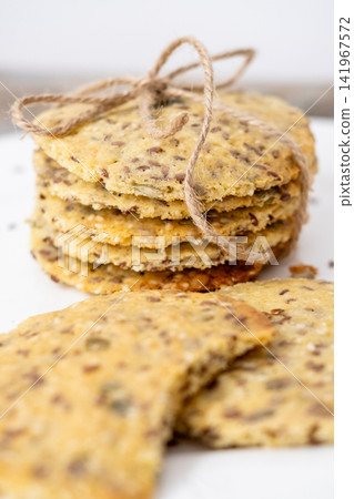 Homemade pastry. Organic food. Savory cookies baked with seeds served on white plate. Healthy crispbread pile tied with rope background. Homemade pastry. Organic food. Savory cookies baked with seeds served on white plate. Healthy crispbread pile tied with rope background. 141967572
