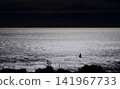 Small sailboat on shimmering sea beneath a dramatic dark sky 141967733