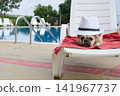 French bulldog wearing white fedora relaxing on poolside sun lounger 141967737