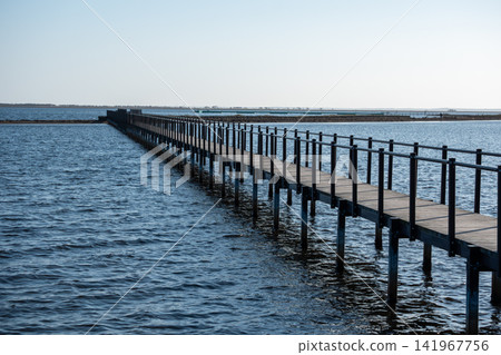 A long wooden pier stretching out into the blue sea 141967756