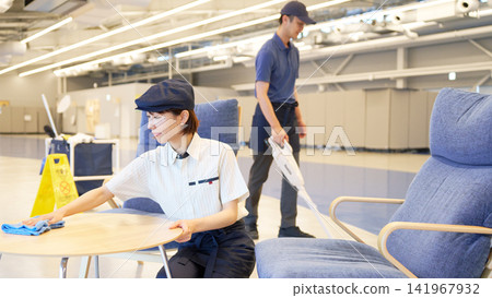Two cleaning staff members, a man and a woman, cleaning tables and floors within the facility. 141967932