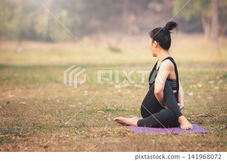 Asian woman practicing yoga on mat in outdoor park. Asian woman practicing yoga on mat in outdoor park. 141968072