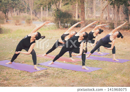 Group of Asian women practicing yoga stretching sideways to start preparing of Prep Poses for Side Crane Pose for Parsva Bakasana on the mat in outdoor park. Group of Asian women practicing yoga stretching sideways to start preparing of Prep Poses for Side Crane Pose for Parsva Bakasana on the mat in outdoor park. 141968075