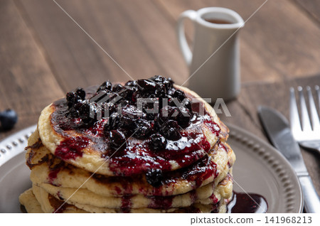 A breakfast scene featuring freshly baked pancakes served with homemade blueberry sauce and syrup. A breakfast scene featuring freshly baked pancakes served with homemade blueberry sauce and syrup. 141968213