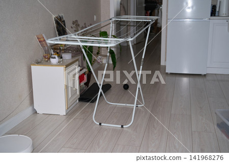 Foldable Drying Rack Standing Indoors Beside Refrigerator And Storage Cabinet In Small Home Foldable Drying Rack Standing Indoors Beside Refrigerator And Storage Cabinet In Small Home 141968276