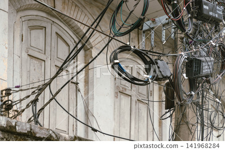 A tangled web of modern cables and coiled fiber optics creates a stark urban contrast against the elegant, vintage arched windows in the background. A tangled web of modern cables and coiled fiber optics creates a stark urban contrast against the elegant, vintage arched windows in the background. 141968284