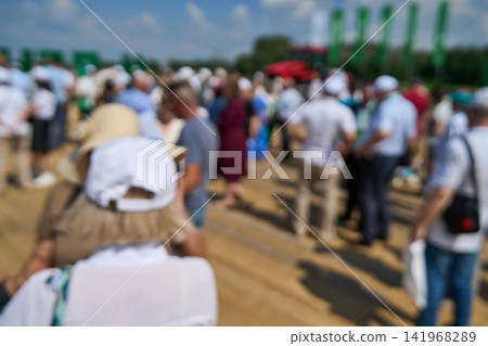 Crowd Attendees Standing On Wooden Outdoor Deck Beneath Blue Sky At Sunny Event With Blurred Crowd Attendees Standing On Wooden Outdoor Deck Beneath Blue Sky At Sunny Event With Blurred 141968289