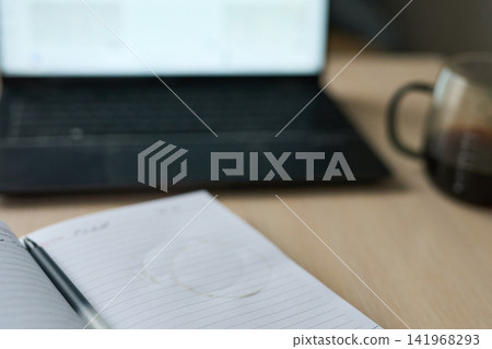 Closeup Lined Notebook Coffee Ring And Pen With Blurred Laptop Keyboard And Glass Mug On Wooden Closeup Lined Notebook Coffee Ring And Pen With Blurred Laptop Keyboard And Glass Mug On Wooden 141968293
