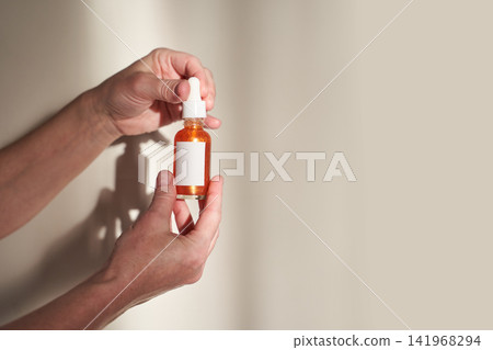 Hands Presenting Labeled Amber Dropper Bottle With White Cap Against Neutral Beige Wall In Studio Hands Presenting Labeled Amber Dropper Bottle With White Cap Against Neutral Beige Wall In Studio 141968294