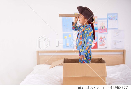 Child, box and pirate hat with spyglasses on bed in home for play, adventure and game as creativity. Boy, cardboard and tricorn with telescope in bedroom for fun, journey and activity as imagination Child, box and pirate hat with spyglasses on bed in home for play, adventure and game as creativity. Boy, cardboard and tricorn with telescope in bedroom for fun, journey and activity as imagination 141968777