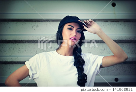 Woman, portrait and cap with street style or wall background in city fashion, cool or confidence. Female person, face and trendy or urban downtown with clothes in New York or grunge, gen z or hat Woman, portrait and cap with street style or wall background in city fashion, cool or confidence. Female person, face and trendy or urban downtown with clothes in New York or grunge, gen z or hat 141968931