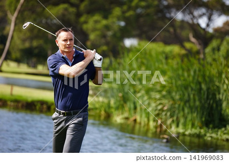 Man, swing and golfer with club by lake for point, score or par shot in outdoor nature. Male person or sports player hitting ball in competition, challenge or practice on grass field or golf course Man, swing and golfer with club by lake for point, score or par shot in outdoor nature. Male person or sports player hitting ball in competition, challenge or practice on grass field or golf course 141969083